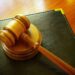 Court gavel rests on a leather binder on a desk.