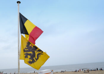 Belgian and Flemish flags fly against a backdrop of an ocean beach