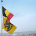 Belgian and Flemish flags fly against a backdrop of an ocean beach